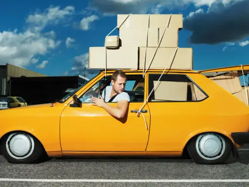 Hombre en coche amarillo cargado de cajas, preguntándose cuanto peso aguanta un coche.