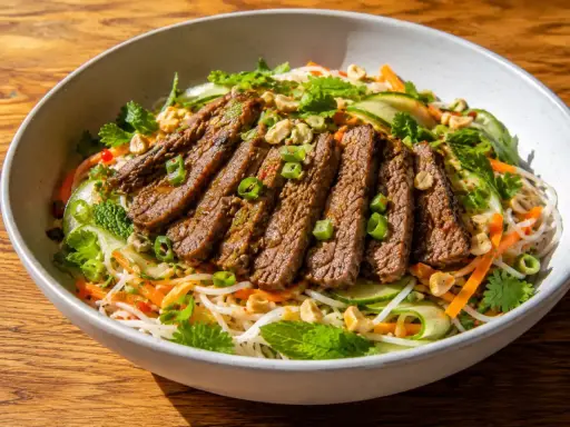 En skål med asiatisk biffsallad med nudlar, strimlad biff, gurka, morötter, mynta och jordnötter.
