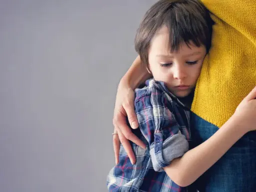 Niño de 6 años abraza a su madre con apego excesivo, buscando consuelo en su abrazo protector.