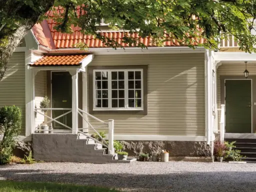 Ett charmigt hus med tegelrött tak och ljusgul fasad, redo att måla om huset. En stor ek skuggar entrén.