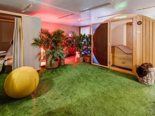 Une salle de pause originale avec un gazon synthétique, une cabine en bois, des plantes et un fauteuil de massage.