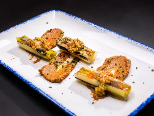 Puerros a baja temperatura, tiernos y dorados, servidos con una sabrosa salsa y granos de mostaza.