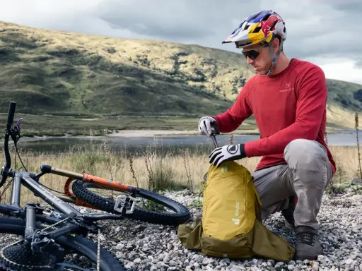 Rowerzysta w kasku przygotowuje żółty plecak Deuter. Idealny, jaki plecak na rower na górskie wyprawy.