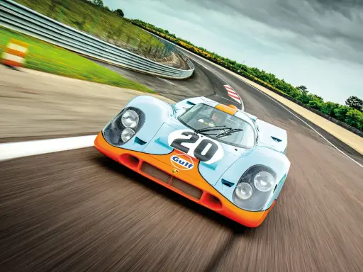 Ein ikonischer Porsche Rennwagen aus den 80ern, der Gulf-Porsche 917, rast auf einer Rennstrecke.