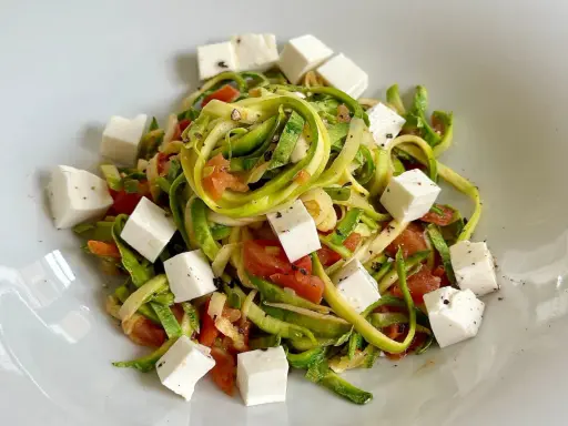 Spaghetti di zucchine freschi con pomodoro e cubetti di feta, conditi con pepe nero.