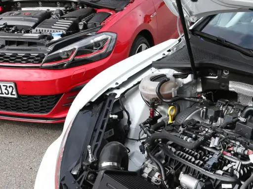 Dos Volkswagen Golf 7 GTI, uno rojo y otro blanco, con capós abiertos mostrando sus motores.