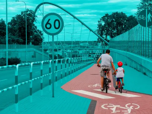 Ojciec i syn na rowerach jadą ścieżką rowerową. Obowiązują przepisy dla rowerzystów, w tym ograniczenie prędkości do 60 km/h.