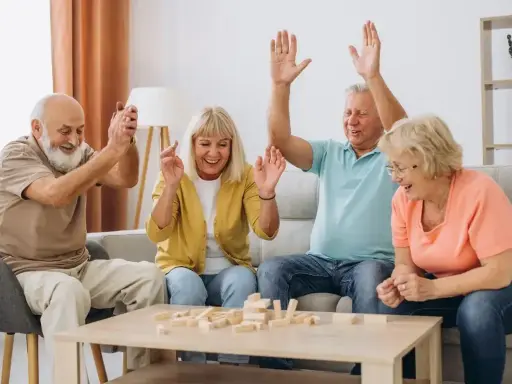 Radosna terapia zajęciowa dla seniorów: czworo uśmiechniętych osób gra w Jengę, unosząc ręce w geście zwycięstwa lub ekscytacji.