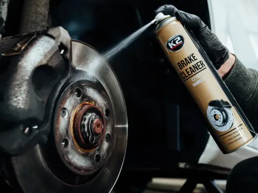 Ręka w czarnej rękawiczce rozpyla środek K2 Brake Cleaner na zużyte tarcze hamulcowe, usuwając brud i rdzę.