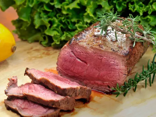 Saftiges Roastbeef mit perfekter kerntemperatur medium, garniert mit Rosmarin. Daneben ein Zitronen- und Salatblatt.