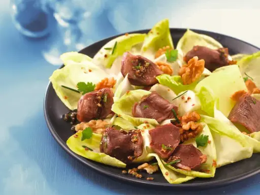 Salade de gésiers savoureuse avec endives croquantes, noix et persil frais, assaisonnée d'une vinaigrette aux graines.