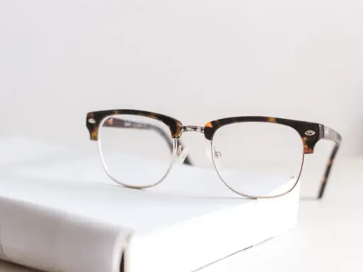 Okulary w stylu retro leżą na białej książce. Zastanawiasz się, od ilu dioptrii trzeba nosić okulary?