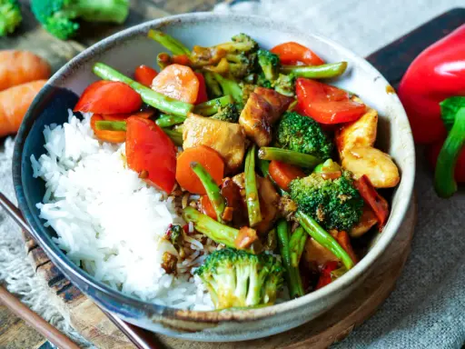 Schüssel mit Reis und einem bunten Chop Suey aus Hühnchen, Brokkoli, Karotten, Paprika und grünen Bohnen.