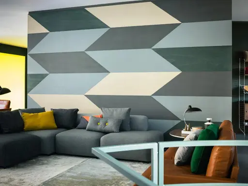 Un salon moderne avec un canapé gris et un mur orné d'un motif géométrique audacieux. Une idée motif peinture murale qui crée une illusion de profondeur.