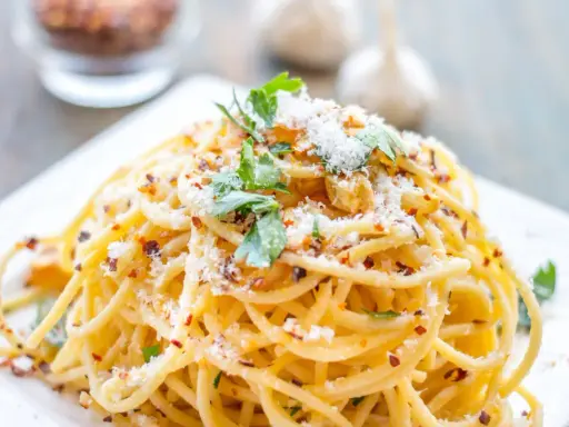 Pyszne spaghetti aglio olio, posypane parmezanem i natką pietruszki, z płatkami chili w tle.