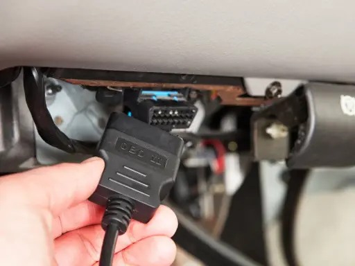 Ręka podłącza kabel OBD II do złącza diagnostycznego pojazdu, aby sprawdzić błędy DTC.