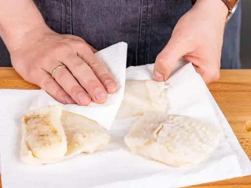 Hände tupfen Steinbeißer Fischfilets auf Küchenpapier trocken, bereit für die Zubereitung.