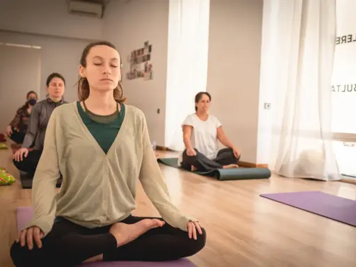 Mujeres meditando en clase de yoga. Una de ellas, en primer plano, parece estar en el **primer trimestre de embarazo**, buscando calma y conexión.
