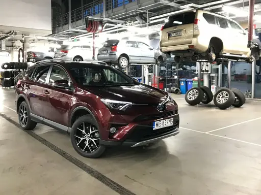 Czerwona Toyota RAV4 w serwisie. W tle inne auta na podnośnikach. Zastanawiasz się nad toyota trzeci przegląd gwarancyjny cena?