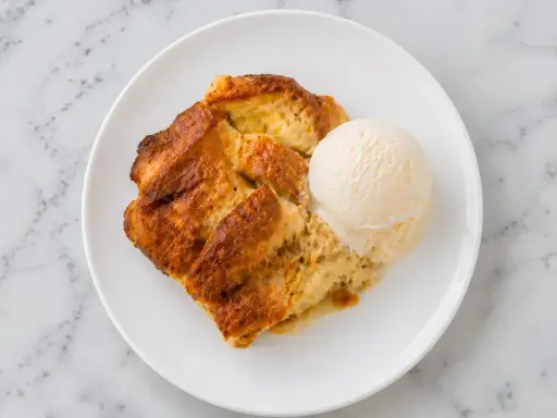 Un délicieux pain perdu au four, doré et moelleux, servi avec une boule de glace à la vanille sur une assiette blanche.
