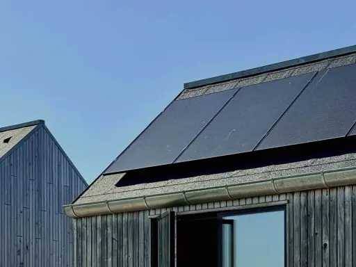 Mörka träfasader möter tak med solpaneler. En modern, hållbar design som fångar solens energi, nästan som en denim solar-dröm.