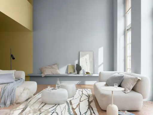 Sala de estar con paredes en tonos grises y mostaza, muebles claros y alfombra con diseño orgánico. Ideales colores suaves para pintar una casa.