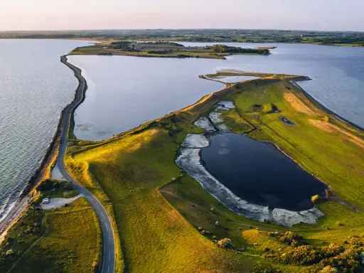 Grönskande landskap med en slingrande väg längs kusten i Danmark. En vy som från ett utkikstorn Danmark, med vatten och fält.