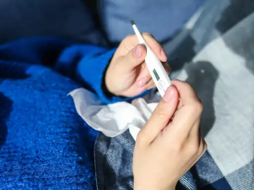 Dłonie trzymające termometr, chusteczki i niebieski sweter. Może to być objaw choroby, np. liszajec ICD-10.