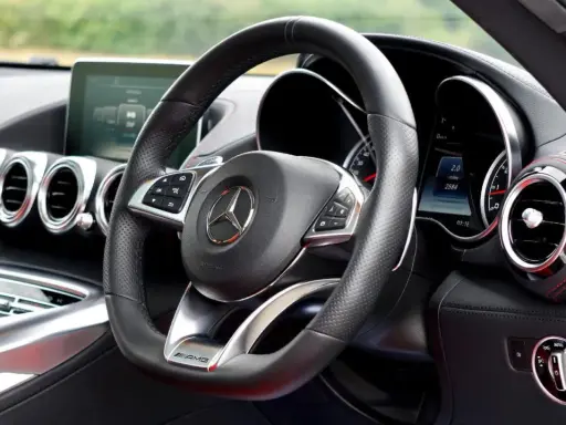 Interior de un coche deportivo Mercedes-AMG. Volante de cuero negro con controles, logo de Mercedes y detalles AMG.