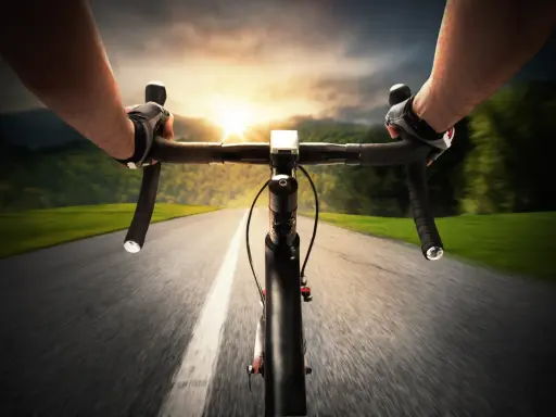 Rowerzysta w rękawiczkach pędzi po asfalcie. Słońce zachodzi, a krajobraz rozmywa się w tle. Ile czasu zajmie mu przejechanie 100 km rowerem?