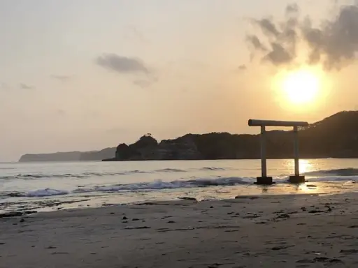 Zachód słońca nad spokojnym morzem, z bramą torii na plaży w Japonii.