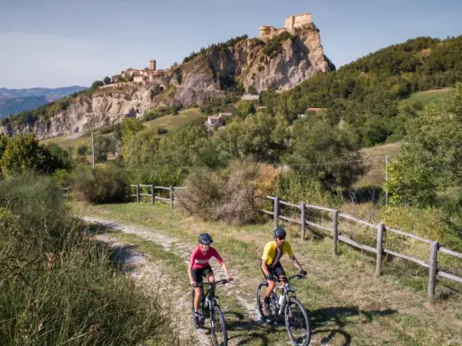 Ciclisti su una ciclabile panoramica con un borgo fortificato in lontananza, un'avventura tra le colline vicino a Rimini.