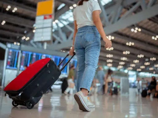 Kobieta z walizką na lotnisku, sprawdza swoją listę na wyjazd.