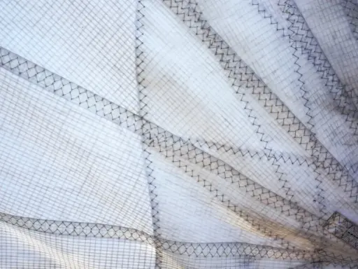 Nahaufnahme eines weißen Segels mit sichtbaren Nähten und Gittermuster. Das Segel reinigen ist wichtig für die Langlebigkeit.