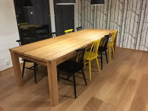 Stilleben matbord i trä med svarta och gula stolar. Bakom syns en fondvägg med trädmotiv.