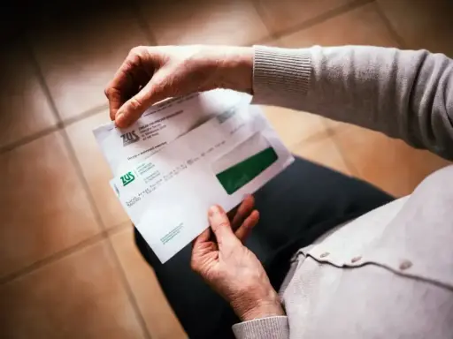 Dłonie trzymają kopertę ZUS. W środku decyzja o waloryzacji emerytury, być może zapowiedź trzynastej emerytury.