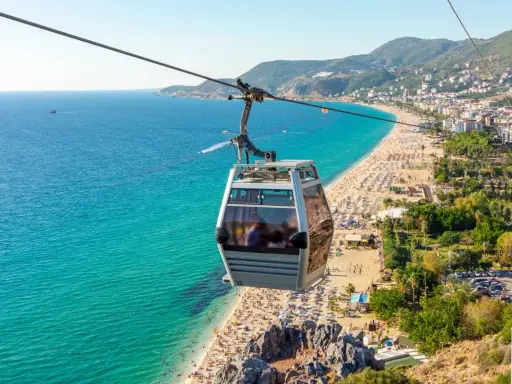 Seilbahn über dem belebten Alanya Strand mit türkisfarbenem Meer und vielen Sonnenanbetern.