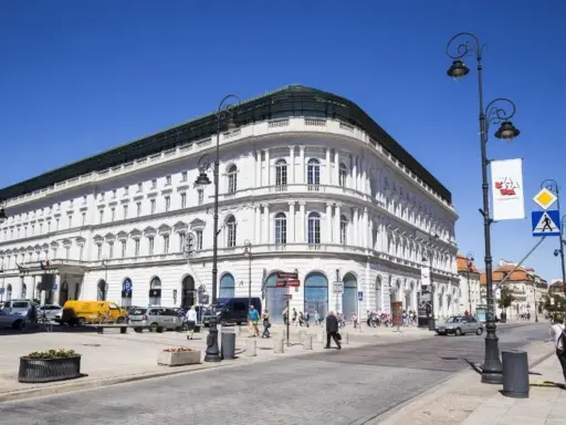 Elegancki, biały budynek w centrum Warszawy, być może najdroższy hotel w Warszawie. Słoneczny dzień, ruch uliczny.