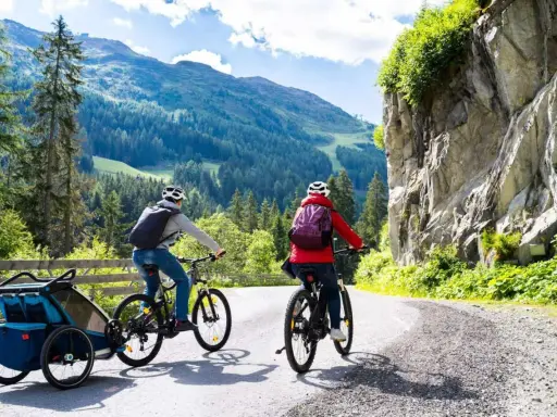 Zwei Radfahrer mit Rucksäcken und Anhänger fahren auf einer Bergstraße.