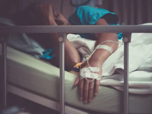 Pacjent w łóżku szpitalnym, z kroplówką, cierpiący. Może to być objaw wstrząsu septycznego, kod ICD-10 A41.