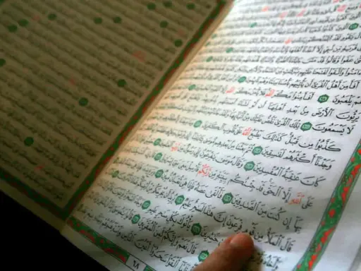 Ein Finger zeigt auf eine Seite des Korans. Die Frage, wer hat den Koran geschrieben, wird durch die heiligen Schriften beantwortet.