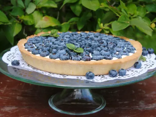 Pyszna tarta z borówkami, udekorowana listkami mięty, prezentuje się apetycznie na szklanej paterze.
