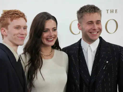Skådespelare från "The Crown" ler glatt. En man med rött hår i mörk kavaj, en kvinna i ljus tröja och en man i mönstrad kavaj.