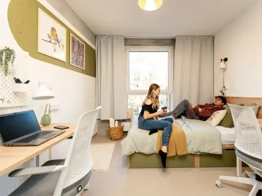 Dwoje studentów w pokoju, marzących o darmowych studiach zaocznych. Na biurku laptop, na łóżku relaks.