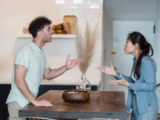 Pareja discutiendo en la cocina, un momento de reflexiones de pareja en crisis. Sus gestos y expresiones muestran tensión.
