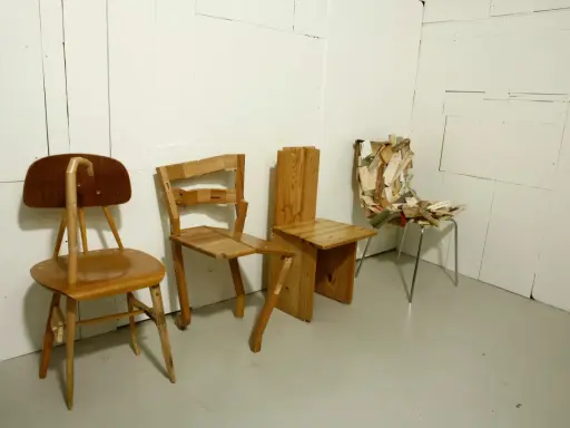 Tre unika stolar står uppradade. En av dem, med en böjd rygg, påminner om en design av Finn Ahlgren.