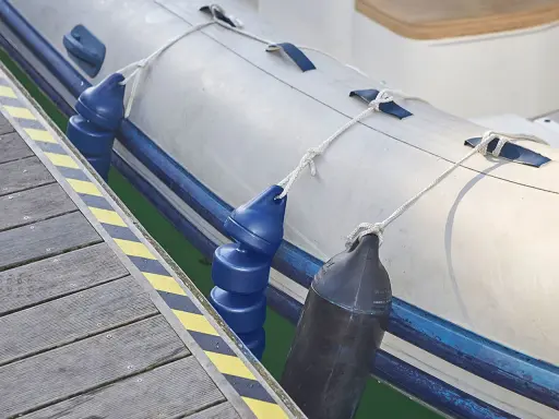 Un bateau pneumatique est amarré à un quai, avec des pare-battages bleus et noirs prêts à gonfler pour protéger la coque.