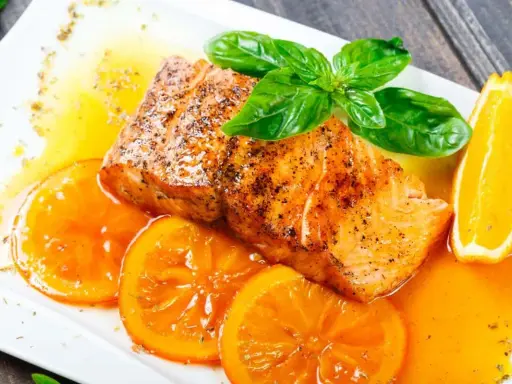 Delicioso salmón a la naranja, jugoso y dorado, servido con rodajas de naranja fresca y una salsa vibrante.