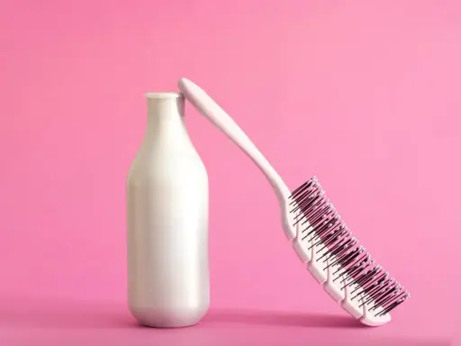 Eine weiße Flasche, die wie ein **collagen shampoo** aussieht, lehnt an einer Haarbürste auf rosa Hintergrund.