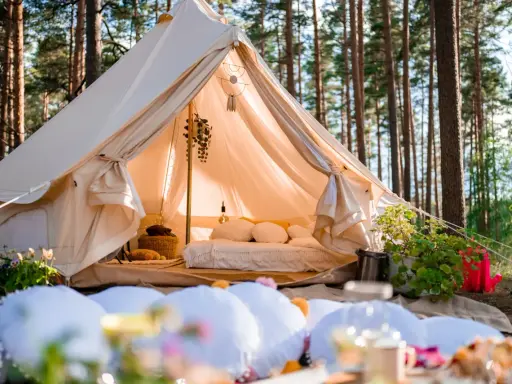 Wygodny namiot w lesie, z łóżkiem i dekoracjami, pokazuje, na czym polega glamping: luksusowy wypoczynek na łonie natury.